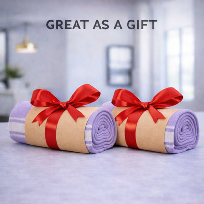 Gift-ready purple towel set of 2 wrapped as two rolls with red ribbon bows on a clean countertop