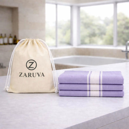 Zaruva lavender bamboo bath towel set of 3 (75x150 cm / 30x60 in), three folded towels stacked beside ZARUVA drawstring pouch on bathroom counter